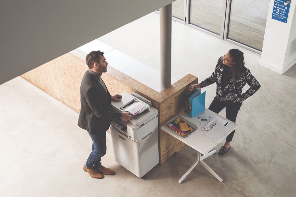 Colleagues stand at a multifunction printer while scanning documents into the cloud.