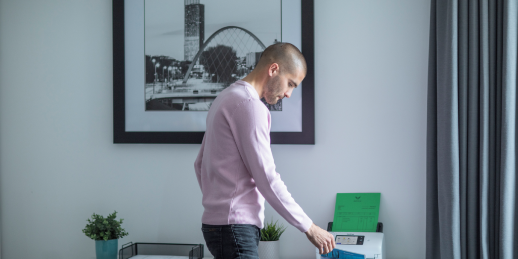 A young man using a desktop document scanner in a home office setting