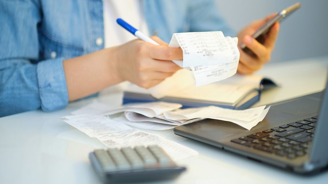 Person with pen, receipt and smartphone in front of laptop calculating home office expenses